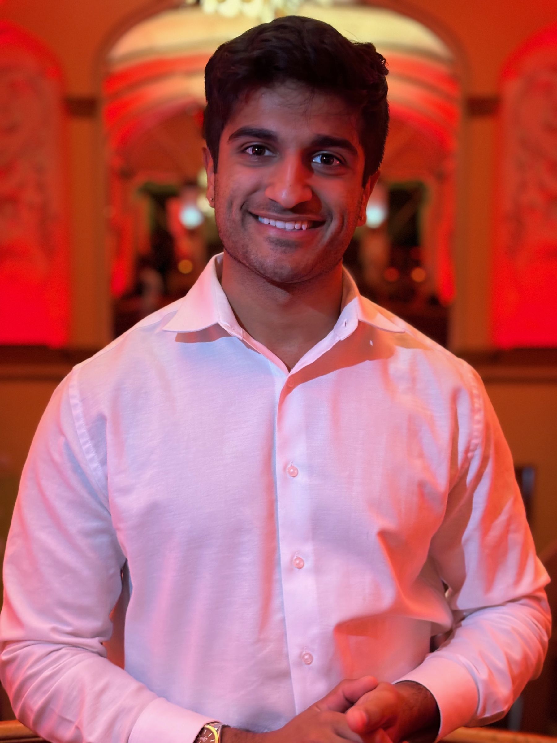 Akku in a white shirt, smiling, in an ornate room lit in red